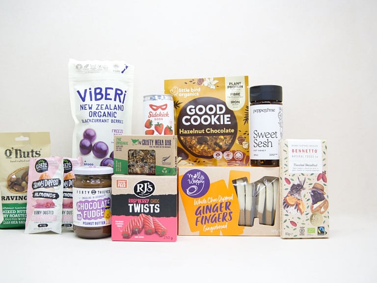 The Great NZ Snack Box featuring gourmet nuts, chocolate almonds, freeze-dried blackcurrants, strawberry soda, artisan chocolate, hot honey, cookies, muesli bars, raspberry twists, and Forty Thieves Chocolate Fudge Peanut Butter, packed with delicious New Zealand-made treats.