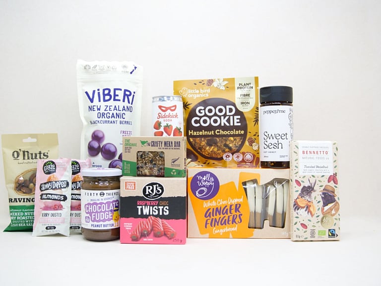 The Great NZ Snack Box featuring gourmet nuts, chocolate almonds, freeze-dried blackcurrants, strawberry soda, artisan chocolate, hot honey, cookies, muesli bars, raspberry twists, and Forty Thieves Chocolate Fudge Peanut Butter, packed with delicious New Zealand-made treats.