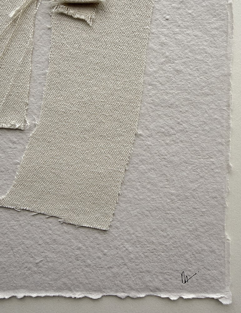 close-up image of handmade sand-toned cotton rag paper with deckled edge and visible surface texture, showing layered repurposed oat-toned cotton fragments, visible weave texture, soft frayed edges and handwritten signature in lower right corner