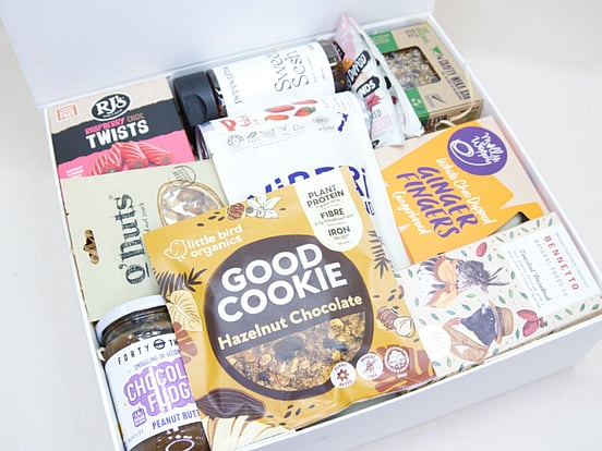 The Great NZ Snack Box featuring gourmet nuts, chocolate almonds, freeze-dried blackcurrants, strawberry soda, artisan chocolate, hot honey, cookies, muesli bars, raspberry twists, and Forty Thieves Chocolate Fudge Peanut Butter, packed with delicious New Zealand-made treats.