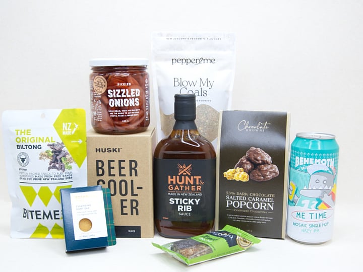 The BBQ Bloke Gift Box featuring Behemoth Me Time craft beer, a HUSKI beer cooler, Hunt & Gather Sticky Rib Sauce, Pepper & Me Blow My Coals seasoning, BiteMeat jerky, Chocolate Brown popcorn, Botanicals body bar, Pure Delish bar, and PICKLED sizzled onions, thoughtfully curated for BBQ lovers and craft beer fans.