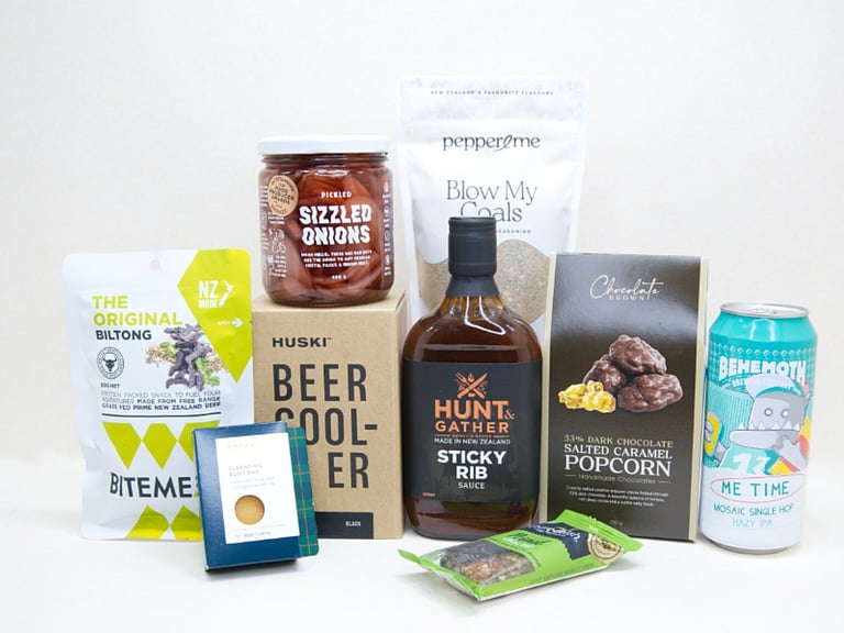 The BBQ Bloke Gift Box featuring Behemoth Me Time craft beer, a HUSKI beer cooler, Hunt & Gather Sticky Rib Sauce, Pepper & Me Blow My Coals seasoning, BiteMeat jerky, Chocolate Brown popcorn, Botanicals body bar, Pure Delish bar, and PICKLED sizzled onions, thoughtfully curated for BBQ lovers and craft beer fans.