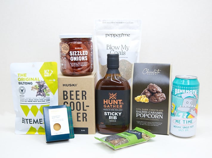 The BBQ Bloke Gift Box featuring Behemoth Me Time craft beer, a HUSKI beer cooler, Hunt & Gather Sticky Rib Sauce, Pepper & Me Blow My Coals seasoning, BiteMeat jerky, Chocolate Brown popcorn, Botanicals body bar, Pure Delish bar, and PICKLED sizzled onions, thoughtfully curated for BBQ lovers and craft beer fans.