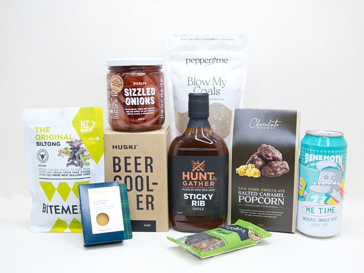 The BBQ Bloke Gift Box featuring Behemoth Me Time craft beer, a HUSKI beer cooler, Hunt & Gather Sticky Rib Sauce, Pepper & Me Blow My Coals seasoning, BiteMeat jerky, Chocolate Brown popcorn, Botanicals body bar, Pure Delish bar, and PICKLED sizzled onions, thoughtfully curated for BBQ lovers and craft beer fans.