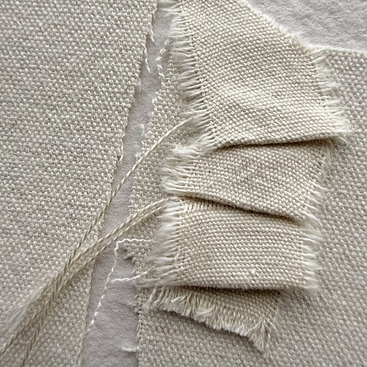 detail image of layered oat-toned cotton fragments and a small cotton fragment hand-stitched into gentle folds, showing visible weave texture, soft frayed edges and hanging threads 