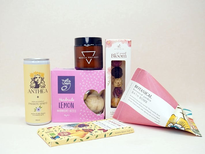 Just Lovely Gift Box featuring Better Tea Co blooming tea balls, Anthea cocktail, Becca Project Stella candle, Botanicals bath bomb, Molly Woppy Lemon Moments, and Bennetto salted caramel chocolate, thoughtfully curated to brighten someone's day and encourage relaxation.