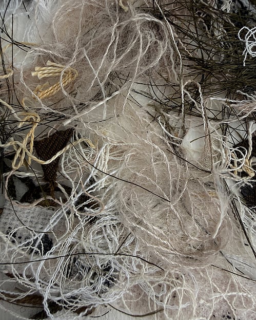 detail image of repurposed yarn, threads and fabric remnants in neutral tones, showing a messy cluster of tangled loops, frayed fibres, varied weave textures and soft frayed fibres