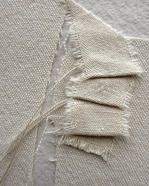detail image of layered oat-toned cotton fragments and a small cotton fragment hand-stitched into gentle folds, showing visible weave texture, soft frayed edges and hanging threads