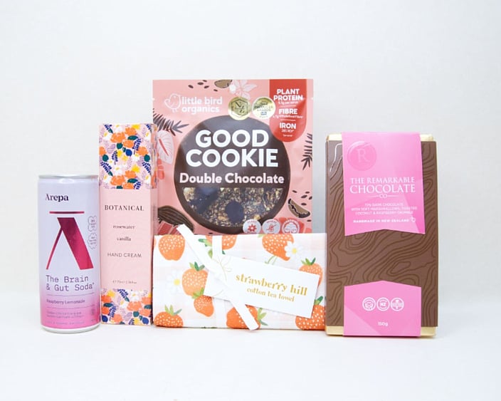 The Pretty in Pink Gift Box featuring an Ārepa Raspberry Lemonade Brain Drink, Botanicals Rosewater & Vanilla Hand Cream, Little Bird Good Cookie, Strawberry Hill Tea Towel, and The Remarkables Marshmallow, Coconut & Raspberry Chocolate, beautifully curated for gifting in New Zealand.
