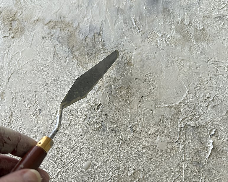 image of artist&rsquo;s hand holding palette knife beside textured 009 / 2026 work in progress