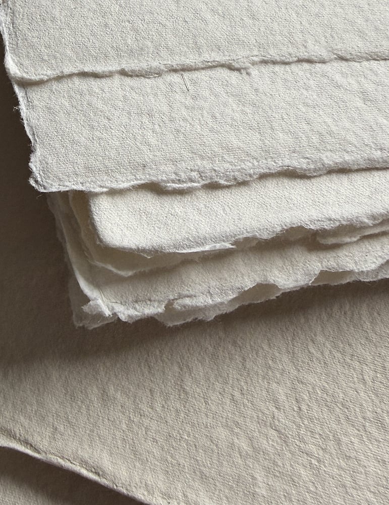 image of stacked sand-toned handmade cotton rag paper with irregular deckled edges