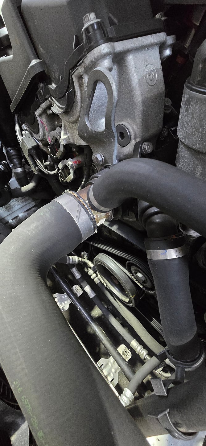 Close view of a deteriorated coolant connection beside the BMW engine