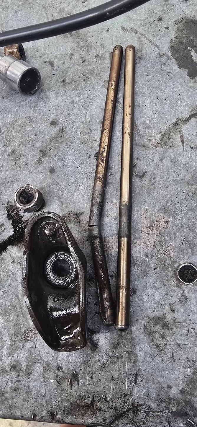 Damaged pushrod beside another pushrod and a rocker arm on the workbench