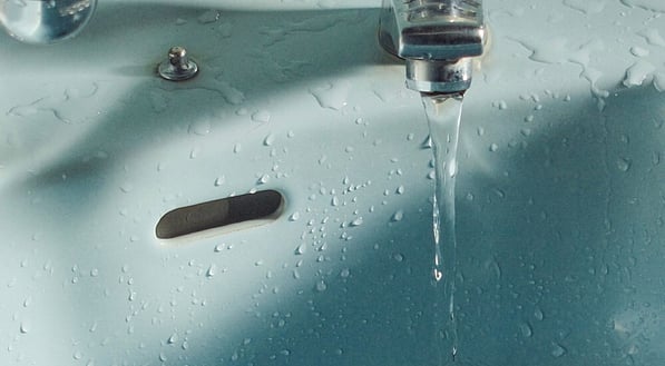 Running tap water streaming into a light blue ceramic sink basin and down the open drain.