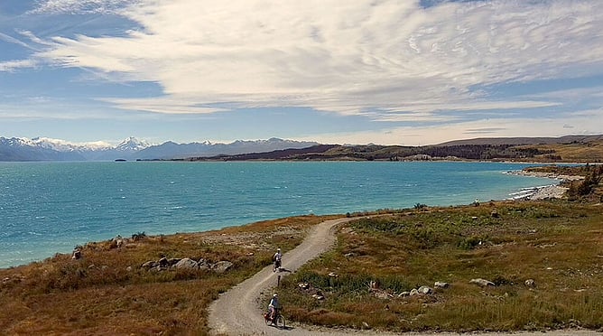 Cyclists on the Alps 2 Ocean trail beside Lake Pukaki, Aoraki Mount Cook ahead, South Island, New Zealand