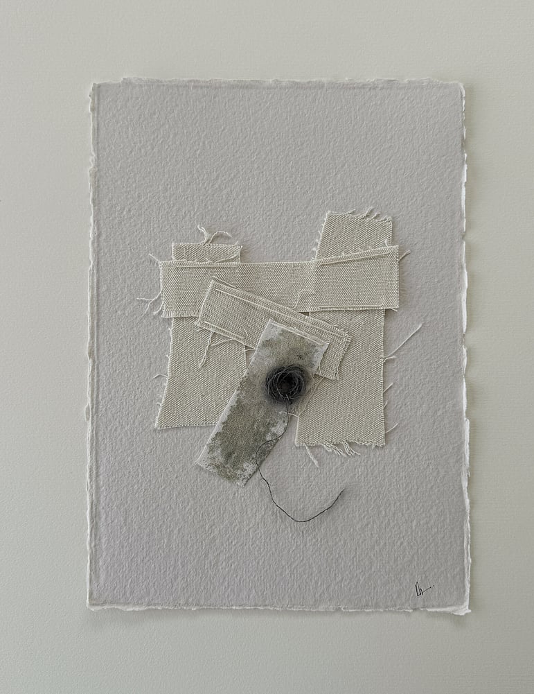 full image of a layered collage on sand-toned handmade cotton rag paper with deckled edges, showing repurposed oat-toned linen and cotton fragments, one blotted with grey-green acrylic, hand-stitched lines in ecru, soft frayed edges and a swirl of charcoal baby alpaca/silk blend yarn remnant, with handwritten signature in lower right corner 