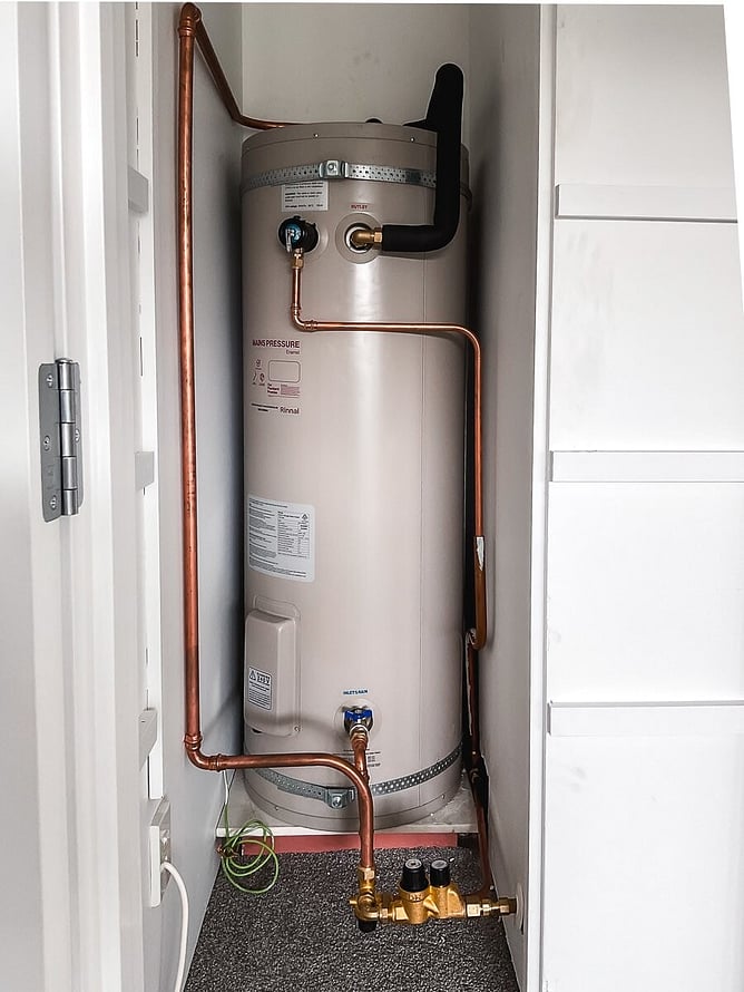 Mains pressure hot water cylinder installed in a cupboard with neat copper pipework and isolation valves at the base.