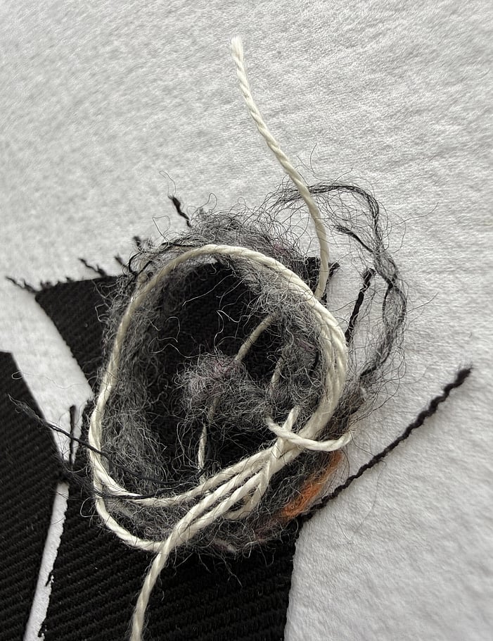 detail image of repurposed black cotton fragments and messy swirl of multi-coloured tweed yarn and trailing ecru thread remnant resting on top, visible weave texture and soft frayed edges 