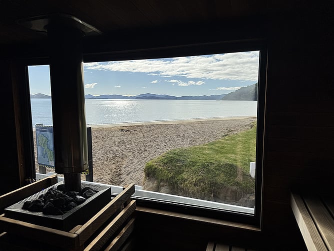 View looking out the large picture window of a wood-fired sauna to the ocean at Long Beach, Russell