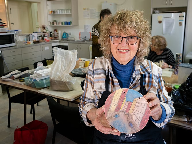 Dot Wilson from Opotiki Arts Society holds a piece of her pottery with other artists in the background. Image credit Anita Burgess