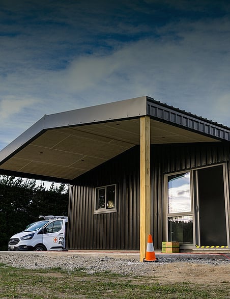 A finished black shed home with a carport under a big Canterbury sky
