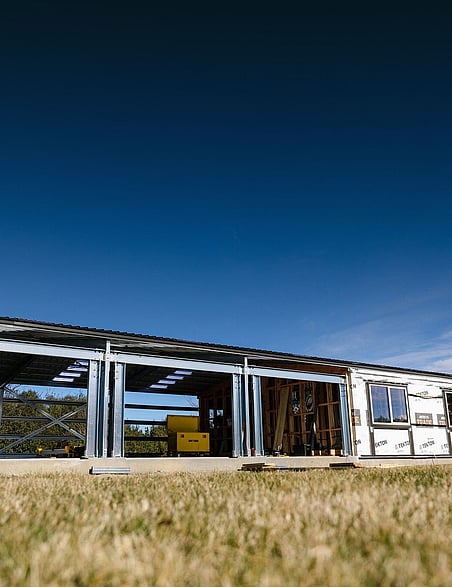 A steel-frame kitset shed home, partly clad, under a blue sky