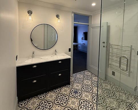 Renovated bathroom with a dark double vanity, round mirror and glass shower enclosure