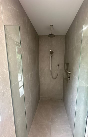 The same shower finished with large grey tiles, a frameless glass panel and a rail shower