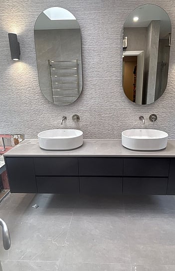 The finished double vanity with wall-hung cabinet, two vessel basins, wall mixers and oval mirrors