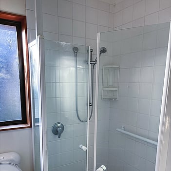 Shower mixer installed behind a glass screen on white tiles
