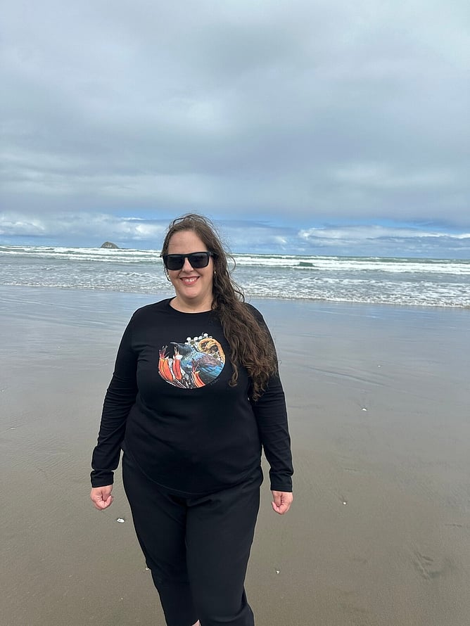 Auckland artist Anna Mollekin smiling on Muriwai Beach in her tūī artwork tee