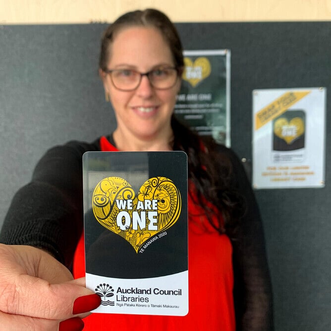 Anna Mollekin holding the We Are One Auckland Libraries card featuring her artwork