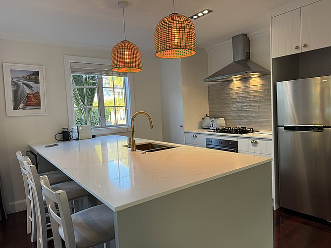 Modern gourmet kitchen at Crab Shack Cottage in Russell featuring stone benchtops, a premium Smeg gas hob and oven, and a brushed brass double sink with an InSinkErator