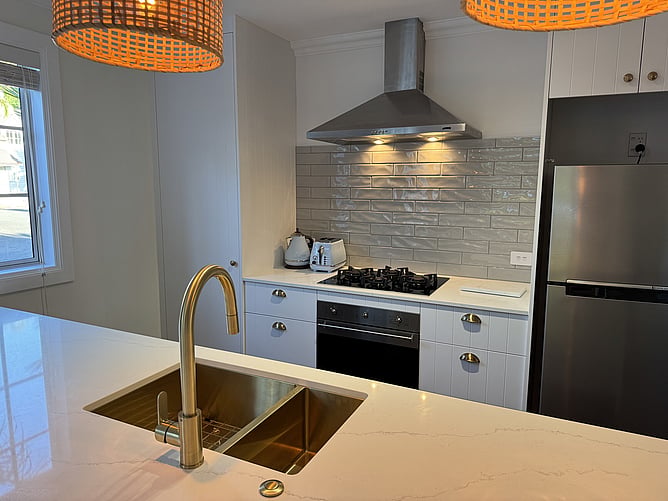Close-up of the modern kitchen at Crab Shack Cottage in Russell showing the brushed brass sink, Smeg gas hob, and white subway tile splashback
