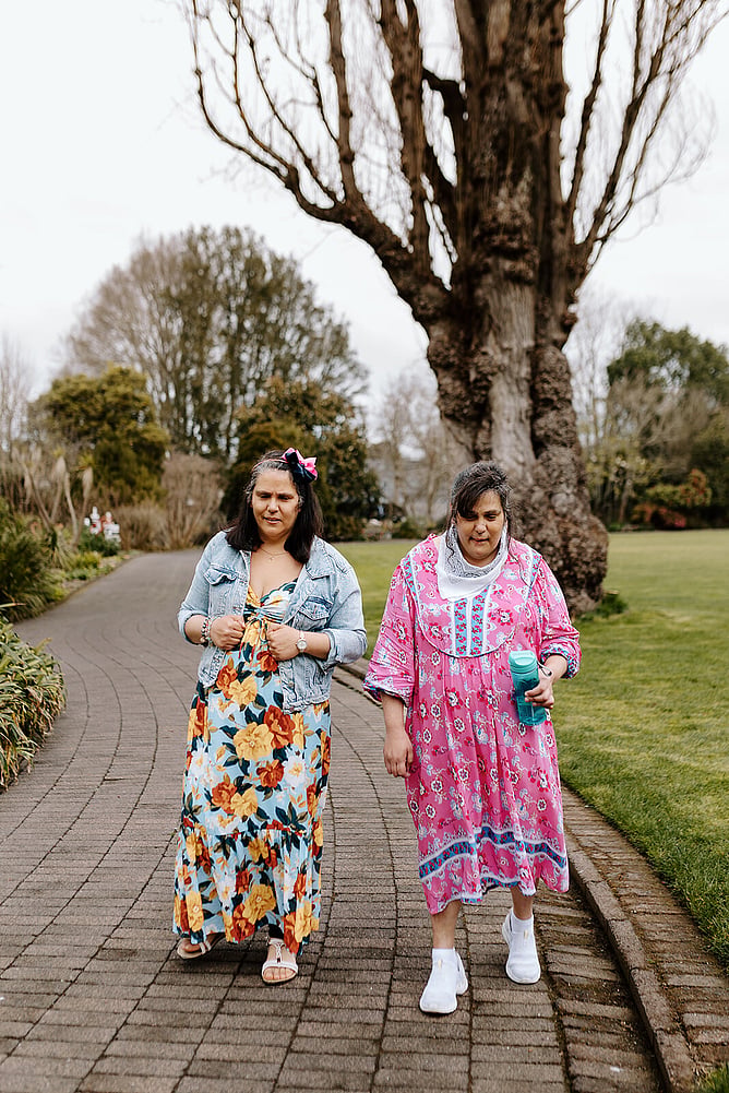 Amanda and Sonia walking together along a garden path beside a large old tree