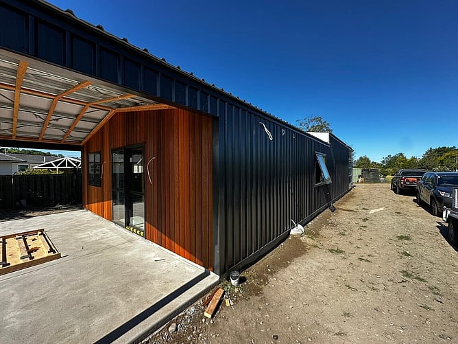 The finished black shed home with a cedar-clad entry, black joinery and a covered patio out front