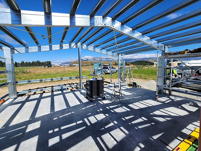 Inside the steel frame, the purlins casting stripes of shadow across the slab, with mountains through the open bay