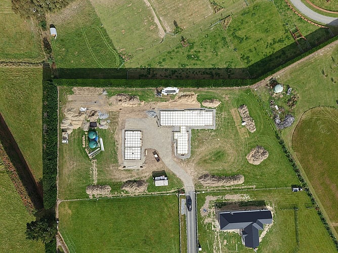 Top-down aerial of the two poured foundation slabs, the water tanks and site sheds in place before framing began