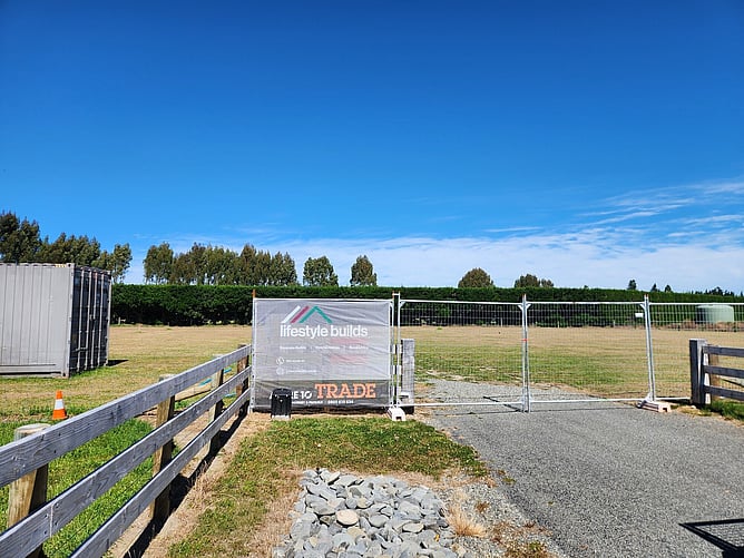 Lifestyle Builds sign on the site fence at the entrance to the Darfield block, shelterbelt behind and a clear blue sky