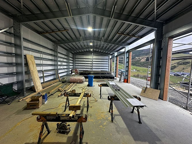 Inside the Henley's steel-framed garage and workshop, saw benches set up on the slab and the Dunedin hills through the open roller door