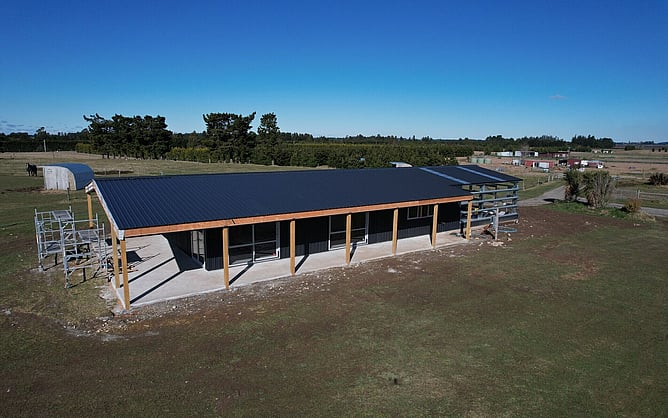 Aerial of the black Oxford shed home with its verandah slab poured, the garage bay still open steel frame and a horse in the paddock beside it