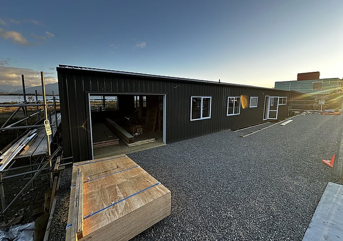 The black-clad Moana bach at dusk with the garage door open and the lake beyond