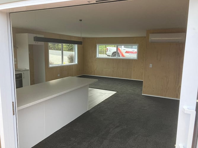 Open-plan living and kitchen with plywood-lined walls and a white island bench