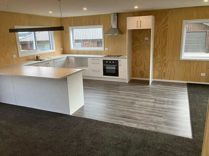 The kitchen in the Moana bach, white cabinetry against plywood walls