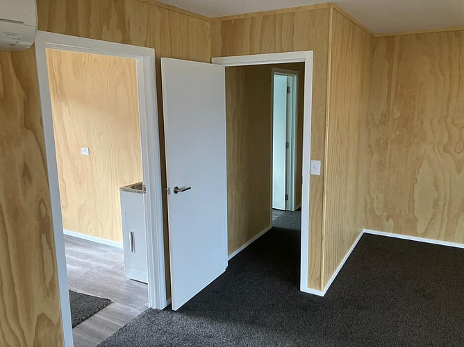 Plywood-lined room inside the bach with doors through to the laundry and the hallway