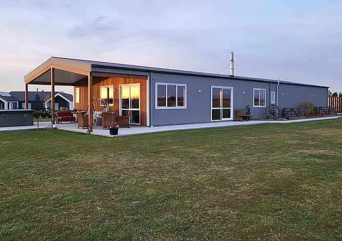 The grey Methven shed home at dusk with its cedar-lined outdoor living area and patio furniture