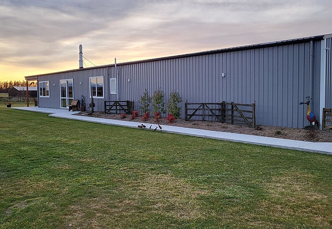 The long grey shed home at sunset with new garden beds planted along the wall