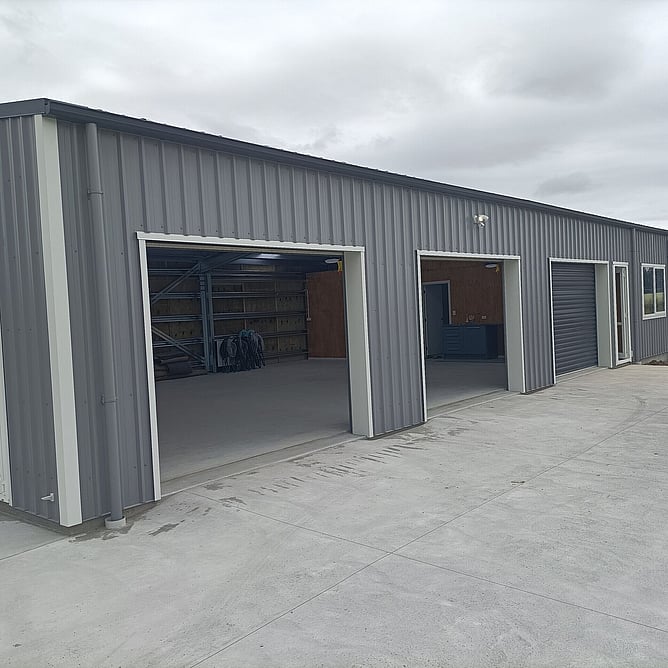 Three garage bays with roller doors on the grey shed home, two of them open