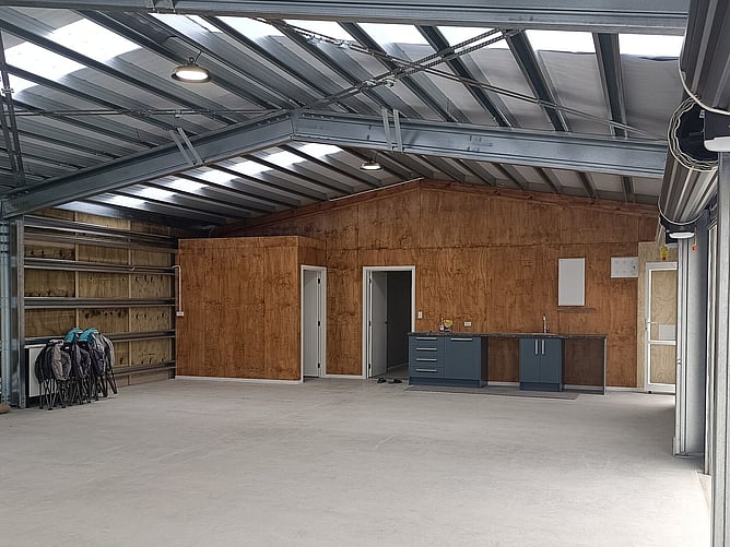 Inside the garage: steel purlins overhead, plywood-lined walls and a kitchenette along the back wall