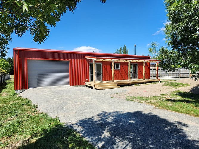 The finished red shed home in Fairlie with its roller door and timber-post verandah
